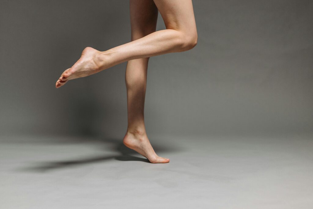 Close-up of a person's legs in an elegant pose on tiptoe against a neutral backdrop.